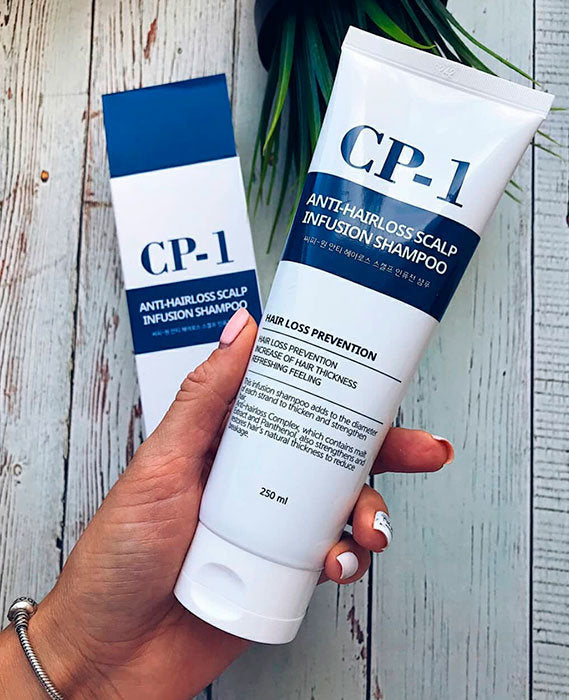 Two bottles of CP-1 Anti-Hairloss Scalp Infusion Shampoo held by a hand against a wooden background.